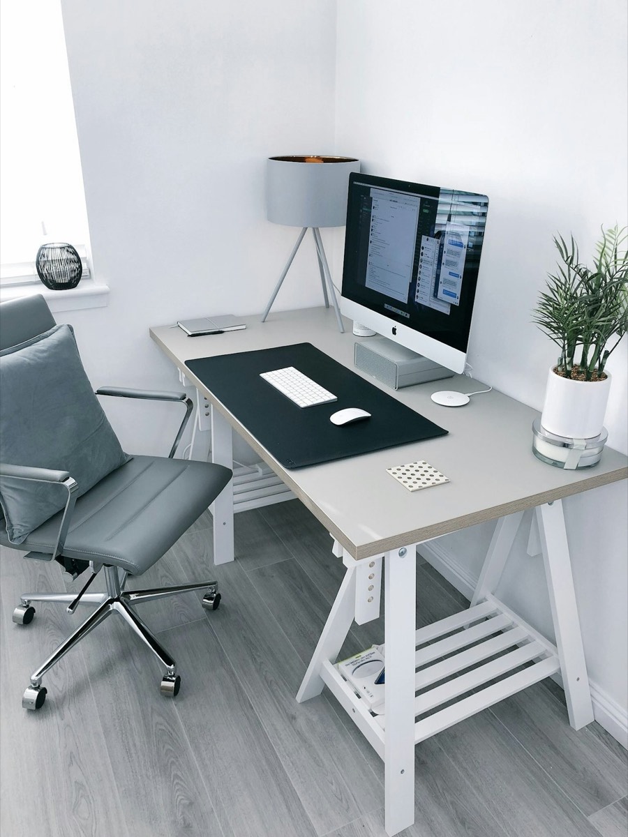 A home office desk with an iMac by a window